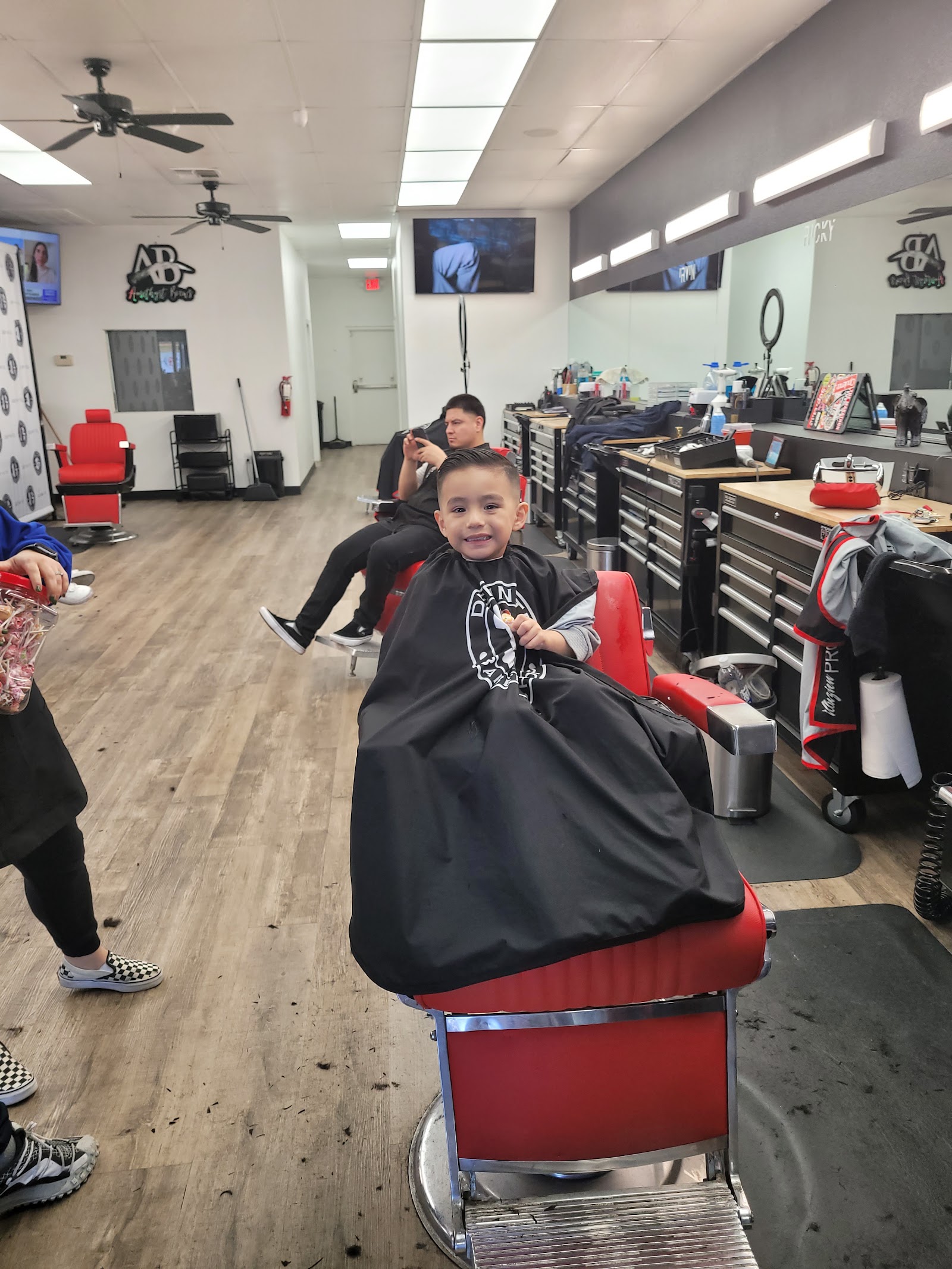 Young boy smiling in a red barber chair inside the busy barbershop