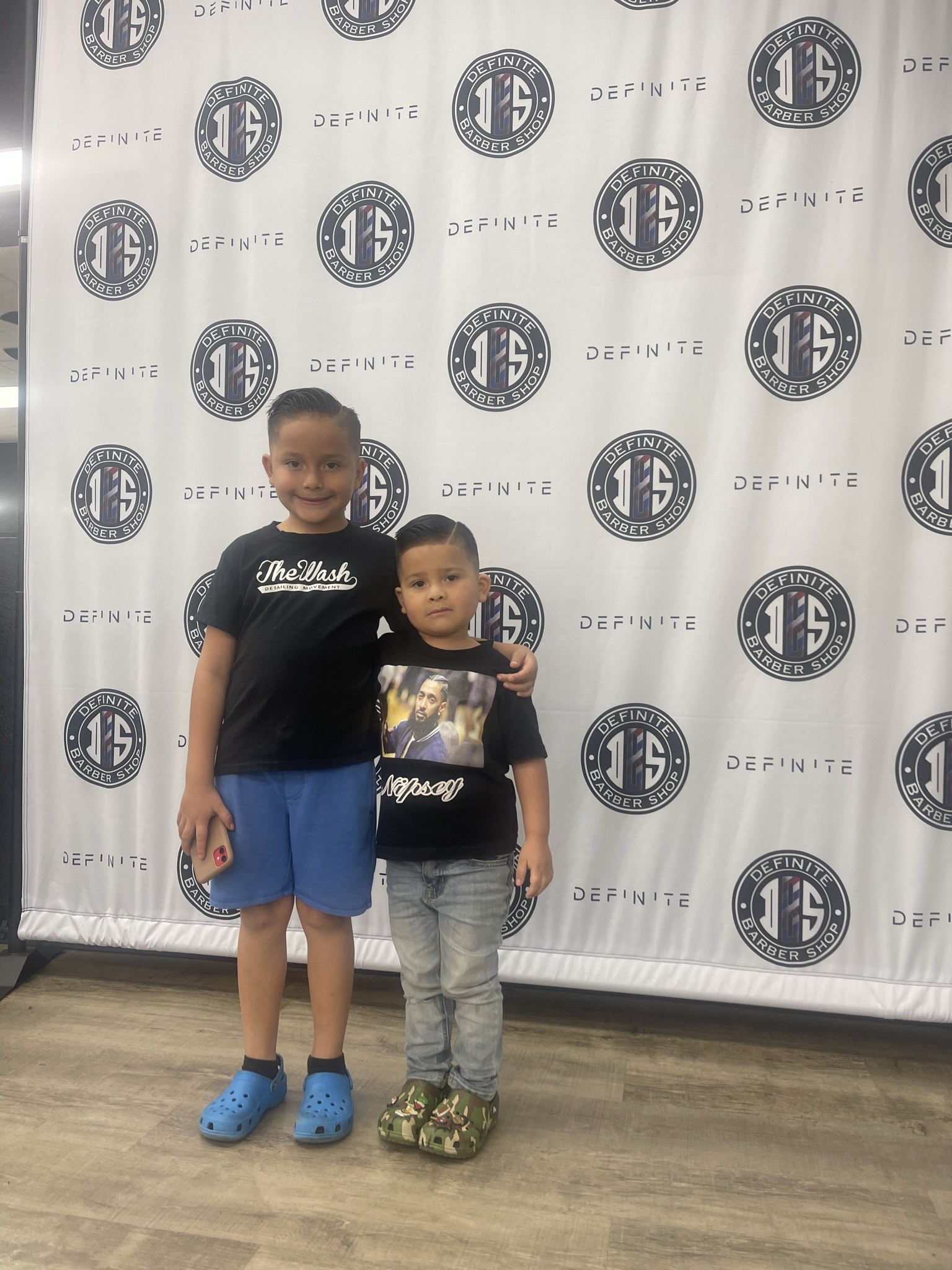 Two boys with fresh haircuts posing in front of the Definite Barber Shop branded backdrop