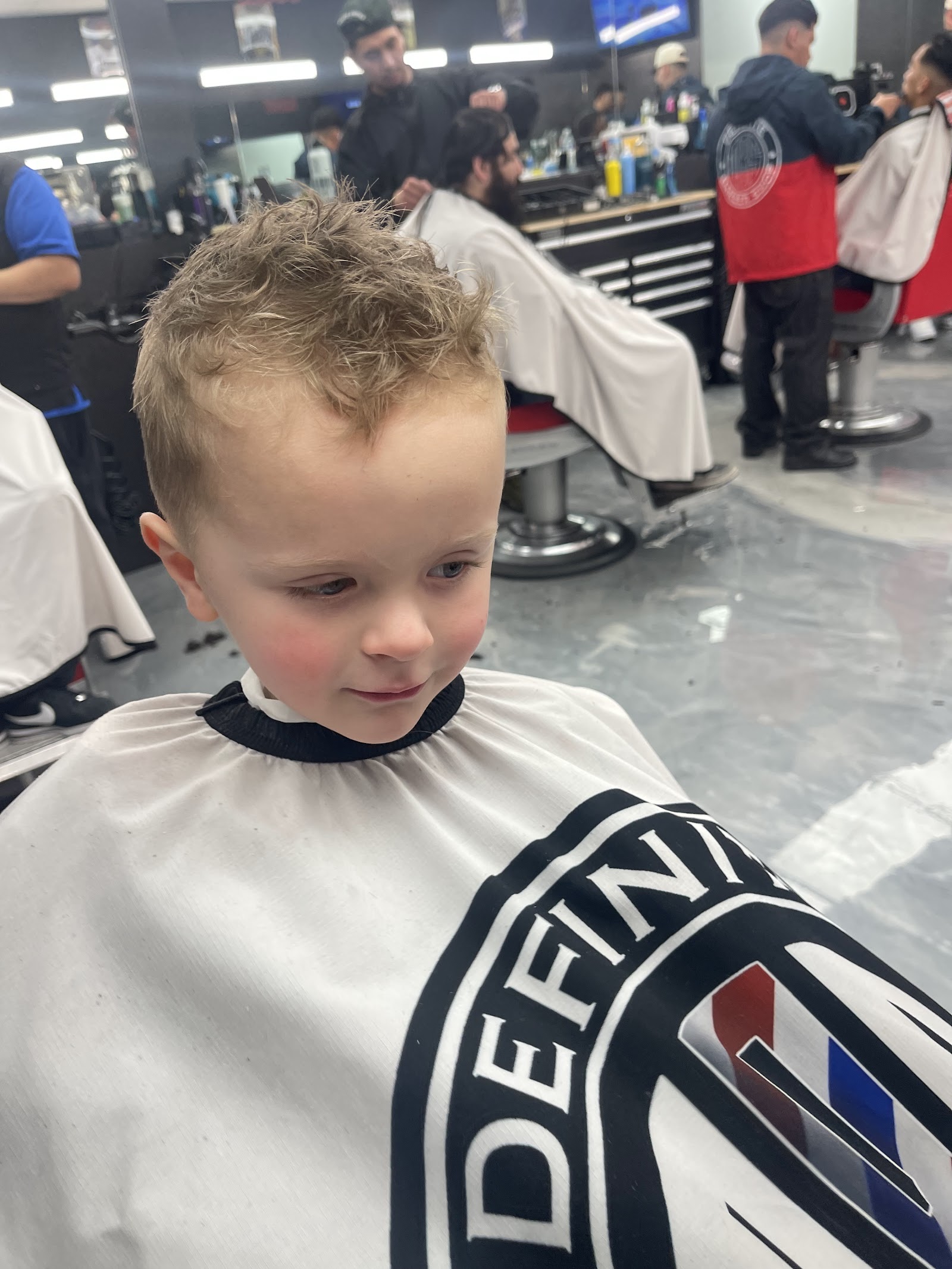 Young blond boy with a fresh textured haircut wearing a Definite cape in the shop